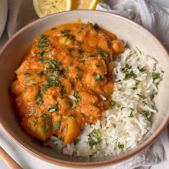 a bowl of chickpea and potato curry, served with white rice and topped with cilantro
